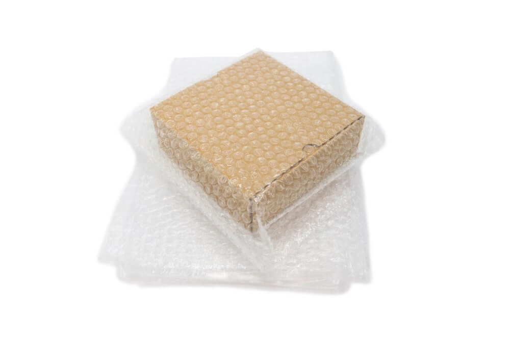 Kartonowe pudełko ułożone na grubej warstwie folii bąbelkowej i dodatkowo nią owinięte – gralapack.com.pl